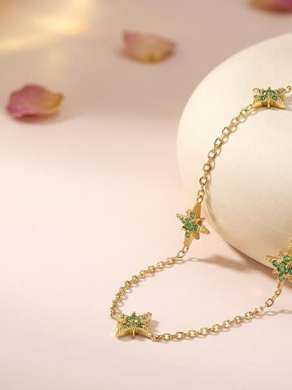Collier doré à motifs étoiles serties de zircons verts, présenté sur un socle crème